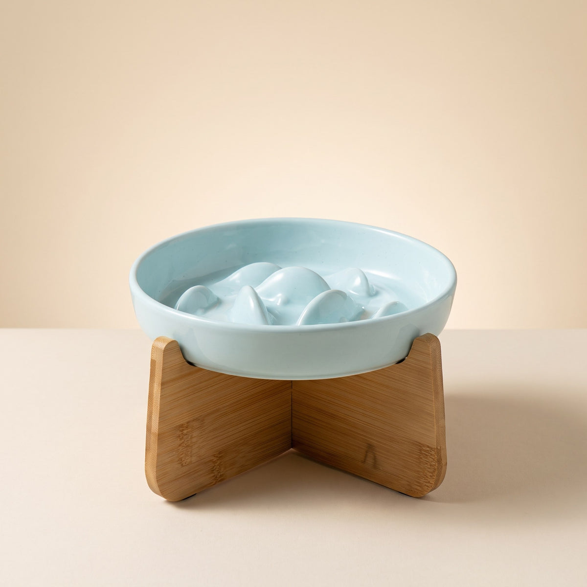Light blue Ceramic Slow Feeder Cat Bowl with maze pattern on a bamboo stand, cream studio background